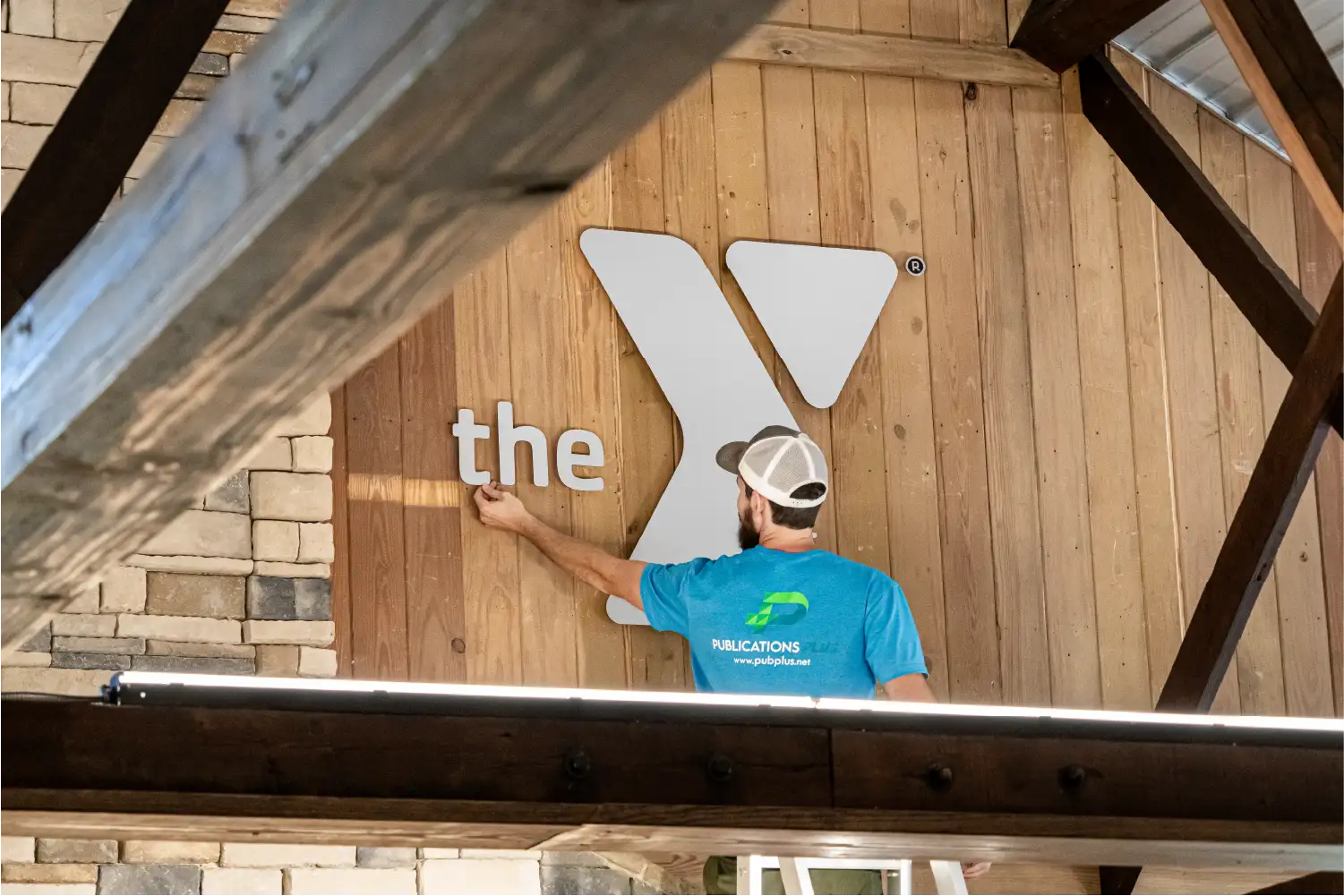 Man on ladder installing silver indoor sign on wooden background