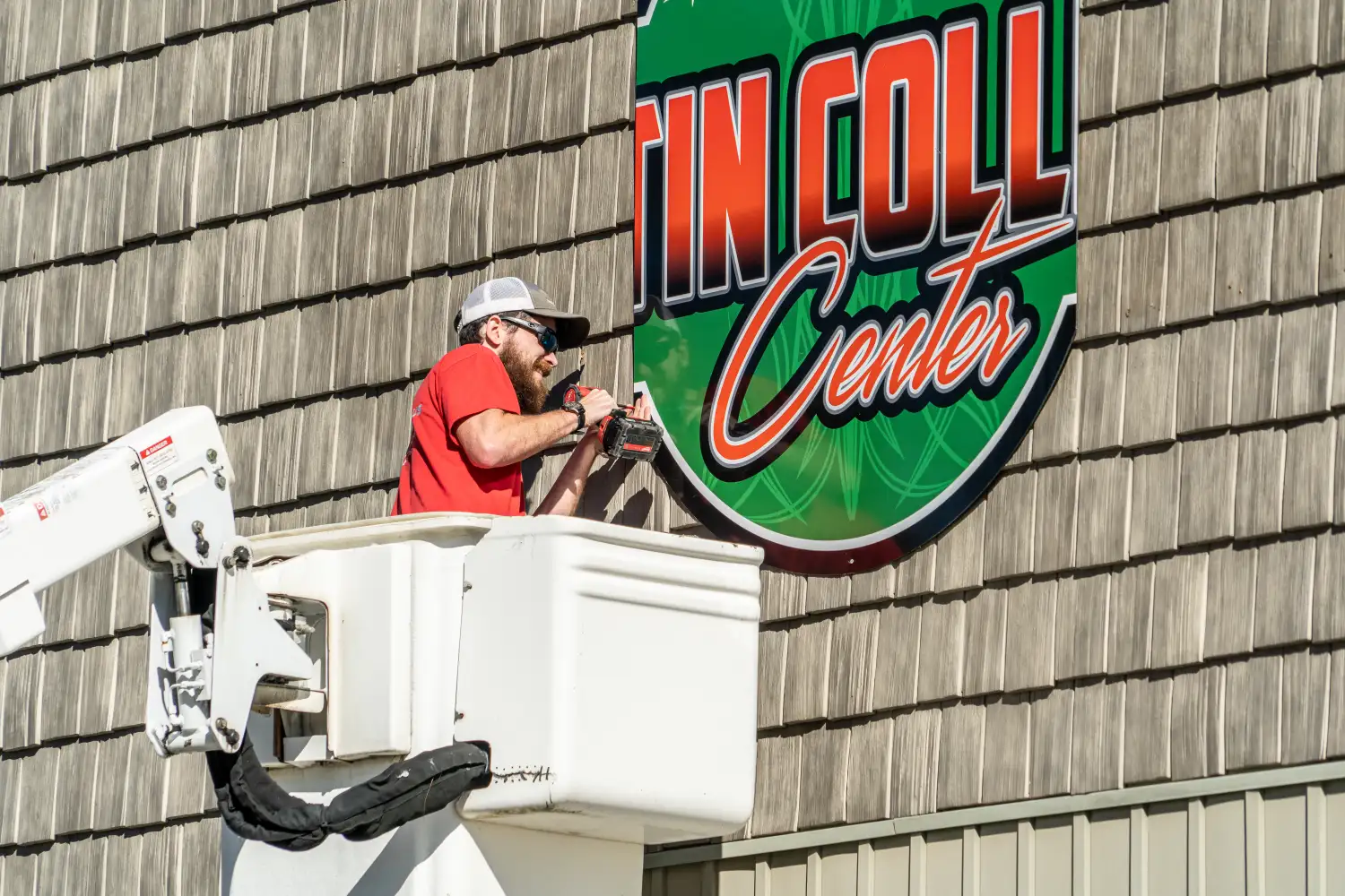 Man in bucket truck installing a green and orange outdoor sign on wooden background