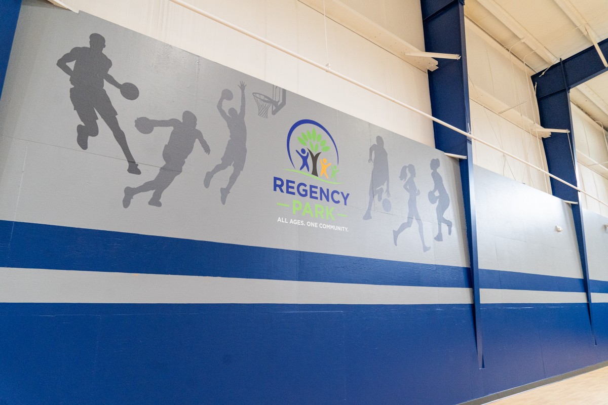 A large mural wall display made of vinyl, featuring people playing basketball and the Regency Park community center logo.