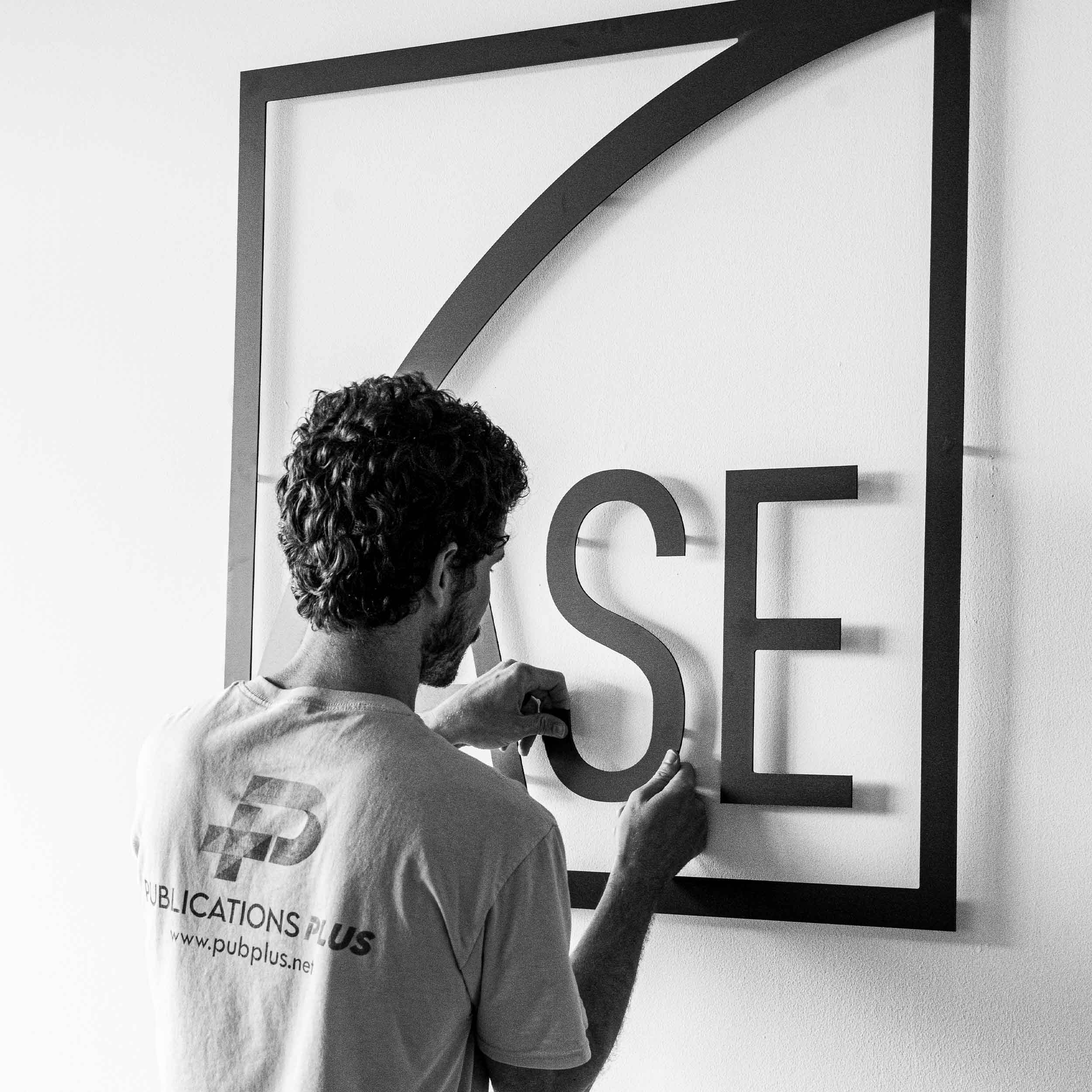 A man installing an interior sign on a white wall